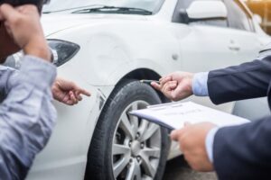 A man holding a clipboard while another man inspects a car