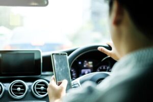 Man driving and using a smartphone with a blank screen in his left hand.